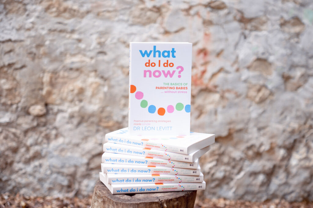 Copies of What Do I Do Now? The basics of parenting babies without stress by Dr Leon Levitt stacked on a stool