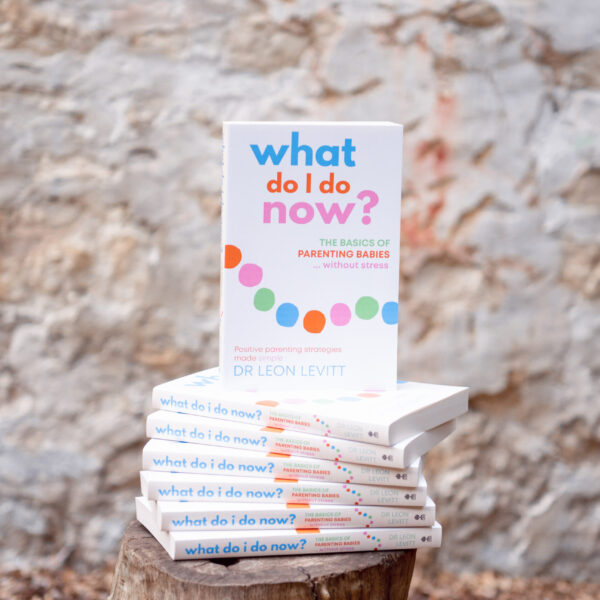 Copies of What Do I Do Now? The basics of parenting babies without stress by Dr Leon Levitt stacked on a stool